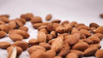 Close-up of almonds being spilled on a white background in slow motion. The nut falls from a height of about 6 inches and lands on the surface with a soft thud. frame rate of 240 frames per second video