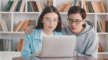 jong vrouw op zoek Bij de laptop en worden verrast en dolblij met haar partner samen in de achtergrond van wit boekenkasten met veel boeken Aan de boekenkasten video