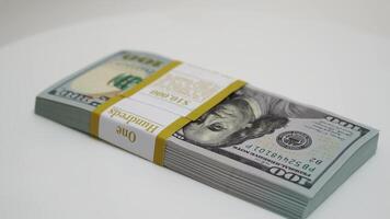 stack of bank bundles with US dollars on a white background. Close-up shot of new, freshly printed hundred-dollar bills rotating on a table. cash flow, business investment, or big money concepts. video