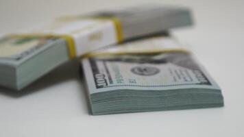 stack of bank bundles with US dollars on a white background. Close-up shot of new, freshly printed hundred-dollar bills rotating on a table. cash flow, business investment, or big money concepts. video