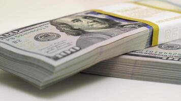 stack of bank bundles with US dollars on a white background. Close-up shot of new, freshly printed hundred-dollar bills rotating on a table. cash flow, business investment, or big money concepts. video