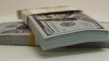 stack of bank bundles with US dollars on a white background. Close-up shot of new, freshly printed hundred-dollar bills rotating on a table. cash flow, business investment, or big money concepts. video