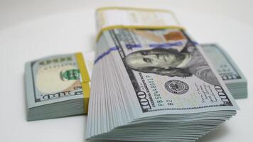 stack of bank bundles with US dollars on a white background. Close-up shot of new, freshly printed hundred-dollar bills rotating on a table. cash flow, business investment, or big money concepts. video