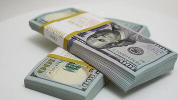 stack of bank bundles with US dollars on a white background. Close-up shot of new, freshly printed hundred-dollar bills rotating on a table. cash flow, business investment, or big money concepts. video