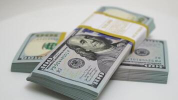 stack of bank bundles with US dollars on a white background. Close-up shot of new, freshly printed hundred-dollar bills rotating on a table. cash flow, business investment, or big money concepts. video