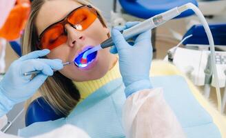 A young beautiful girl in dental glasses treats her teeth at the dentist with ultraviolet light. filling of teeth photo