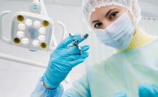 A masked dentist holds an injection syringe for a patient in the office photo