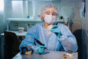 un dental técnico en protector ropa es trabajando en un protésico diente en su laboratorio foto