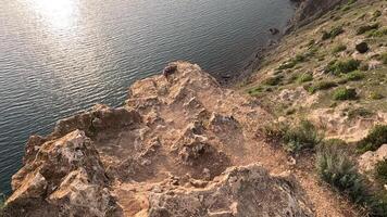 Sonnenuntergang Über Ruhe Meer mit felsig vulkanisch Cliff. abstrakt Natur Sommer- Ozean Meer Hintergrund. klein Wellen auf golden warm Wasser Oberfläche mit Bokeh Beleuchtung von Sonne. schleppend Bewegung video