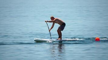 hombre cenar mar. fuerte atlético hombre aprende a paleta cenar en pie en tablero en abierto mar Oceano en soleado día. verano fiesta vacaciones y viaje concepto. aéreo vista. lento movimiento video