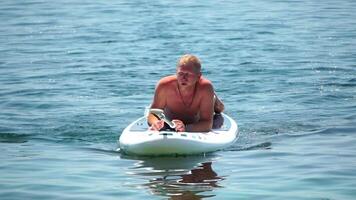 homem sup mar. Forte Atlético homem aprende para remo sup em pé em borda dentro aberto mar oceano em ensolarado dia. verão feriado período de férias e viagem conceito. aéreo visualizar. lento movimento video