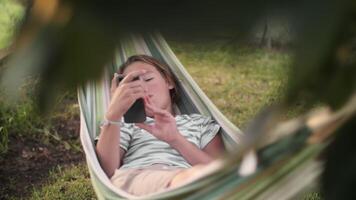 Teenager relaxing in hammock with smartphone video