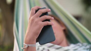 Focused on smartphone in hands of boy in hammock video