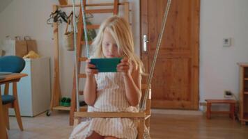 kind swinging Aan binnen- schommel en gebruik makend van smartphone video