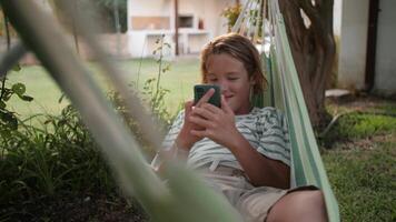 Boy enjoying leisure time with smartphone in hammock video