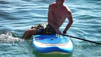 Man Sup Sea. Strong athletic man learns to paddle sup standing on board in open sea ocean on sunny day. Summer holiday vacation and travel concept. Aerial view. Slow motion video