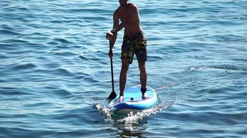 hombre cenar mar. fuerte atlético hombre aprende a paleta cenar en pie en tablero en abierto mar Oceano en soleado día. verano fiesta vacaciones y viaje concepto. aéreo vista. lento movimiento video