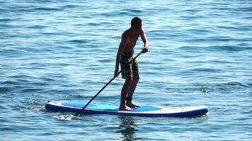 Man Sup Sea. Strong athletic man learns to paddle sup standing on board in open sea ocean on sunny day. Summer holiday vacation and travel concept. Aerial view. Slow motion video