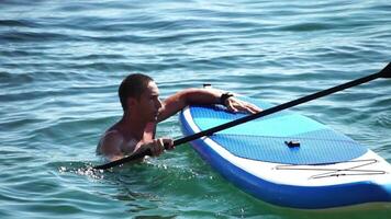 hombre cenar mar. fuerte atlético hombre aprende a paleta cenar en pie en tablero en abierto mar Oceano en soleado día. verano fiesta vacaciones y viaje concepto. aéreo vista. lento movimiento video