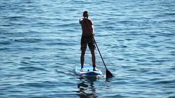 Man Sup Sea. Strong athletic man learns to paddle sup standing on board in open sea ocean on sunny day. Summer holiday vacation and travel concept. Aerial view. Slow motion video