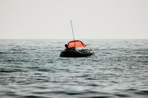 pescador mar bote. turista maniobra un inflable barco mientras pescar en un vida chaqueta, con el hermosa puesta de sol mar en el antecedentes. un relajante pescar viaje. foto