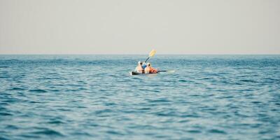 Happy couple kayaks in an inflatable kayak on the sea at sunset. Couple kanoeing in the sea near the island with mountains. People kayaking in life jackets sail. Back view photo