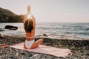 Woman sea yoga. Happy woman in white swimsuit and boho style braclets practicing outdoors on yoga mat by sea on sunset. Women yoga fitness routine. Healthy lifestyle, harmony and meditation photo