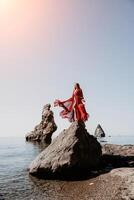 Woman travel sea. Young Happy woman in a long red dress posing on a beach near the sea on background of volcanic rocks, like in Iceland, sharing travel adventure journey photo