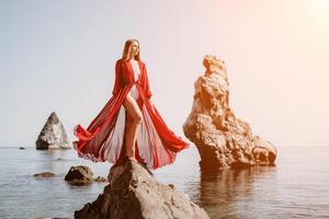 Woman travel sea. Young Happy woman in a long red dress posing on a beach near the sea on background of volcanic rocks, like in Iceland, sharing travel adventure journey photo