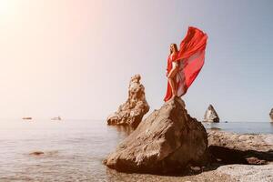 mujer viaje mar. joven contento mujer en un largo rojo vestir posando en un playa cerca el mar en antecedentes de volcánico rocas, me gusta en Islandia, compartiendo viaje aventuras viaje foto