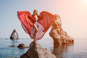 mujer viaje mar. joven contento mujer en un largo rojo vestir posando en un playa cerca el mar en antecedentes de volcánico rocas, me gusta en Islandia, compartiendo viaje aventuras viaje foto