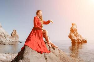 Woman travel sea. Young Happy woman in a long red dress posing on a beach near the sea on background of volcanic rocks, like in Iceland, sharing travel adventure journey photo