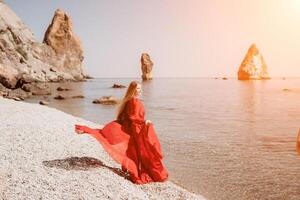 mujer viaje mar. contento turista en rojo vestir disfrutar tomando imagen al aire libre para recuerdos. mujer viajero posando en el rock a mar bahía rodeado por volcánico montañas, compartiendo viaje aventuras viaje foto