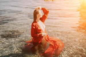 Woman travel sea. Happy tourist in red dress enjoy taking picture outdoors for memories. Woman traveler posing in sea beach, surrounded by volcanic mountains, sharing travel adventure journey photo