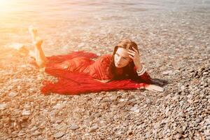 Woman travel sea. Happy tourist in red dress enjoy taking picture outdoors for memories. Woman traveler posing in sea beach, surrounded by volcanic mountains, sharing travel adventure journey photo