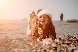 mujer viaje mar. contento turista disfrutar tomando imagen en el playa para recuerdos. mujer viajero en Papa Noel sombrero mira a cámara en el mar bahía, compartiendo viaje aventuras viaje foto