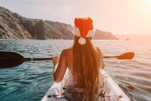 Woman in kayak back view. Happy young woman in Santa hat floating in kayak on calm sea. Summer holiday vacation and cheerful female people relaxing having fun on the boat. photo