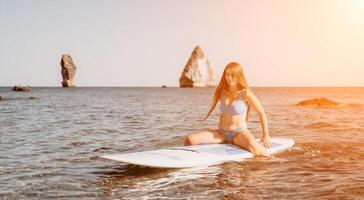 Woman sea sup. Close up portrait of happy young caucasian woman with long hair looking at camera and smiling. Cute woman portrait in a blue bikini posing on sup board in the sea photo