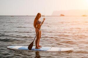 Woman sea sup. Close up portrait of happy young caucasian woman with long hair looking at camera and smiling. Cute woman portrait in a blue bikini posing on sup board in the sea photo