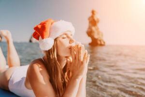 Woman sea sup. Close up portrait of happy young caucasian woman with long hair in Santa hat looking at camera and smiling. Cute woman portrait in a white bikini posing on sup board in the sea photo