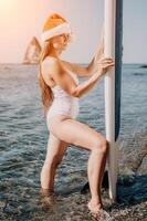 Woman sea sup. Close up portrait of happy young caucasian woman with long hair in Santa hat looking at camera and smiling. Cute woman portrait in a white bikini posing on sup board in the sea photo