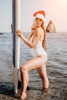 Woman sea sup. Close up portrait of happy young caucasian woman with long hair in Santa hat looking at camera and smiling. Cute woman portrait in a white bikini posing on sup board in the sea photo