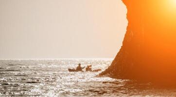 contento Pareja kayaks en un inflable kayac en el mar a puesta de sol. Pareja piragüismo en el mar cerca el isla con montañas. personas kayak en vida chaquetas navegar. espalda ver foto