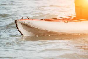 Happy couple kayaks in an inflatable kayak on the sea at sunset. Couple kanoeing in the sea near the island with mountains. People kayaking in life jackets sail. Back view photo