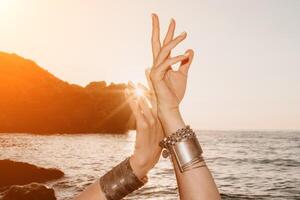 mujer mar yoga. contento mujer en blanco traje de baño y boho estilo pulseras practicando al aire libre en yoga estera por mar en puesta de sol. mujer yoga aptitud rutina. sano estilo de vida, armonía y meditación foto