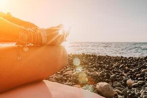 mujer mar yoga. contento mujer en blanco traje de baño y boho estilo pulseras practicando al aire libre en yoga estera por mar en puesta de sol. mujer yoga aptitud rutina. sano estilo de vida, armonía y meditación foto