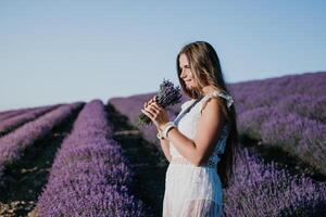 Woman lavender field. Happy carefree woman in a white dress walking in a lavender field and smelling a lavender bouquet on sunset. Ideal for warm and inspirational concepts in wanderlust and travel. photo