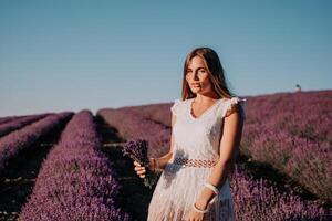 Woman lavender field. Happy carefree woman in a white dress walking in a lavender field and smelling a lavender bouquet on sunset. Ideal for warm and inspirational concepts in wanderlust and travel. photo