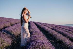 mujer lavanda campo. contento despreocupado mujer en un blanco vestir caminando en un lavanda campo y oliendo un lavanda ramo de flores en puesta de sol. ideal para calentar y inspirador conceptos en pasión de viajar y viajar. foto