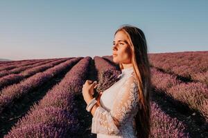 Woman lavender field. Happy carefree woman in a white dress walking in a lavender field and smelling a lavender bouquet on sunset. Ideal for warm and inspirational concepts in wanderlust and travel. photo